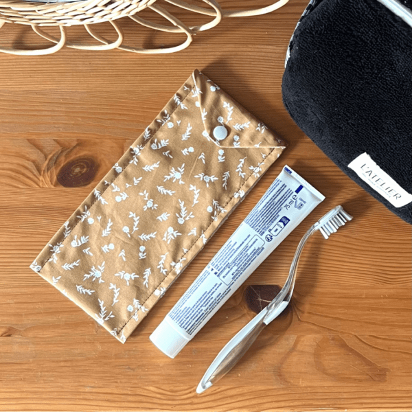 Etui à brosse à dents avec un tissu extérieur de Petites fleurs blanches sur fond camel. Fermeture à l'aide d'un bouton pression blanc.